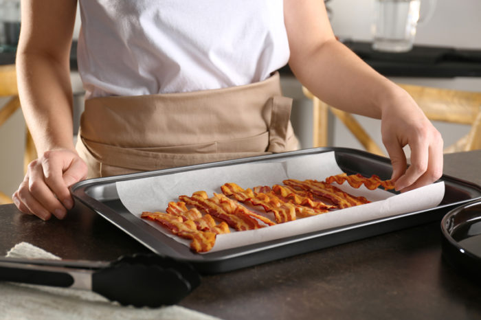 Kvinna med plåt med bacon tillagad i ugn.