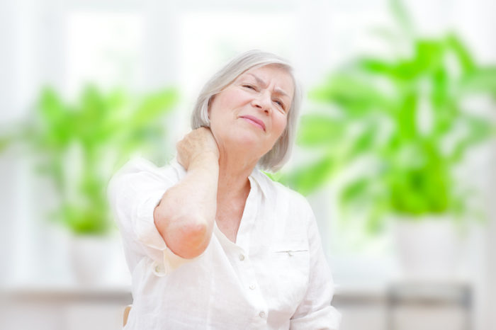 Äldre kvinna med fibromyalgi som tar sig för nacken.