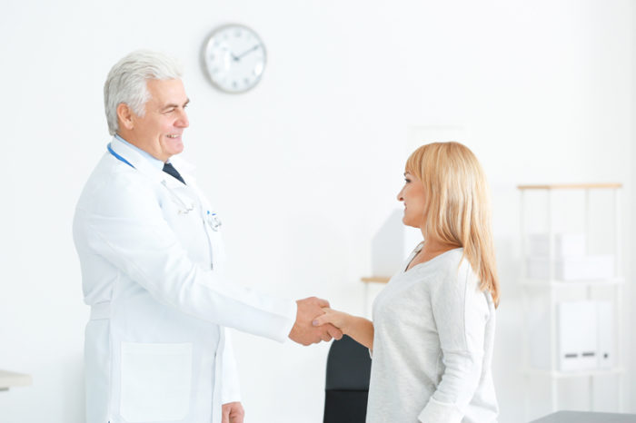Manlig läkare och kvinnlig patient skakar hand.